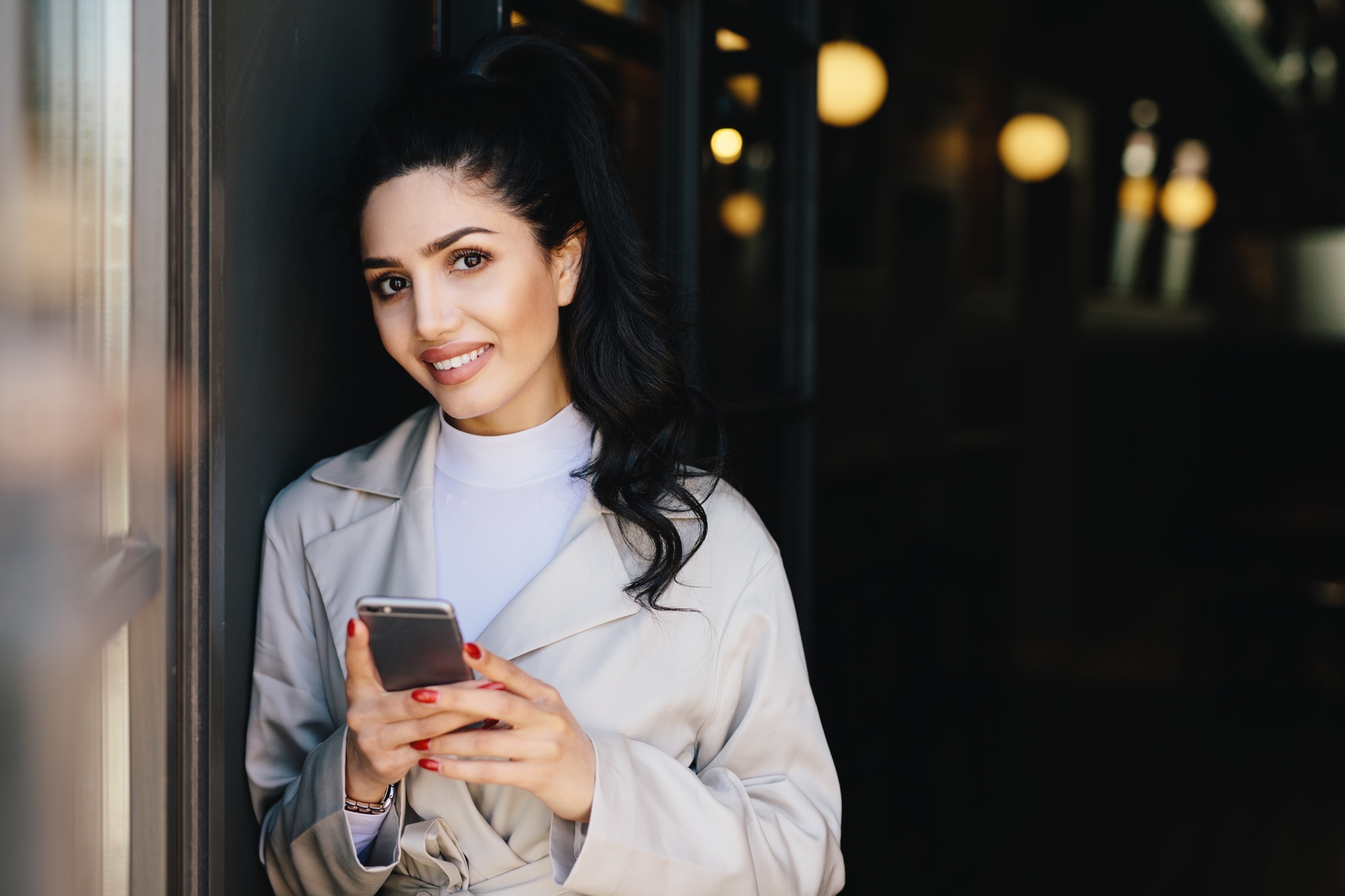 Smiling pretty woman with pony tail dressed formally holding smartphone doing online shopping